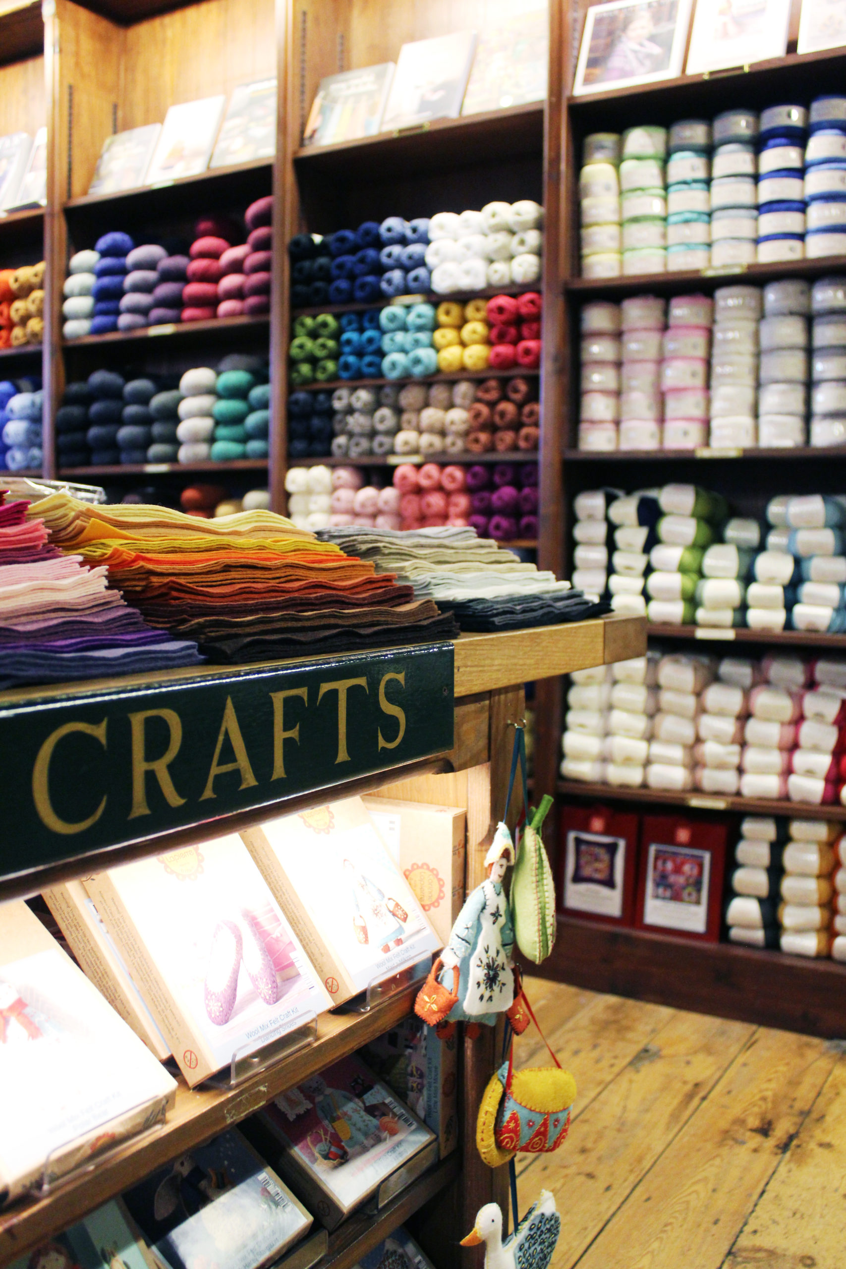 Part of a table and a large bookshelf with various wools, felt etc on display