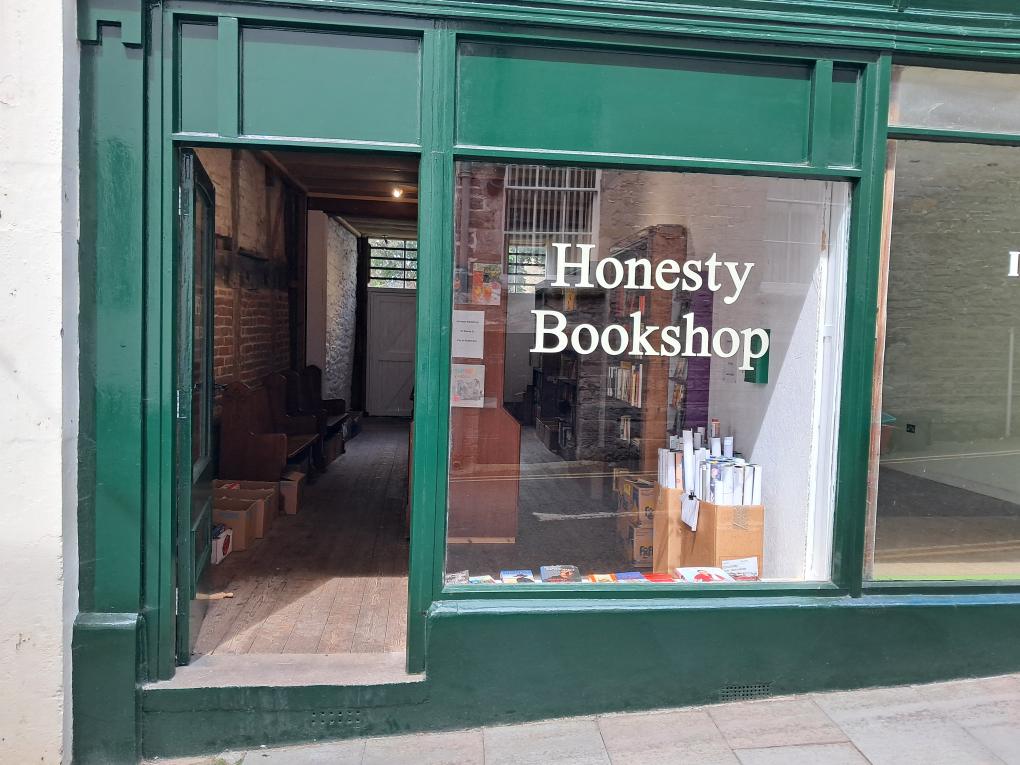 The front of the honesty bookshop. The shop front is dark green, with a large floor to ceiling window that lets you see the bookcases inside