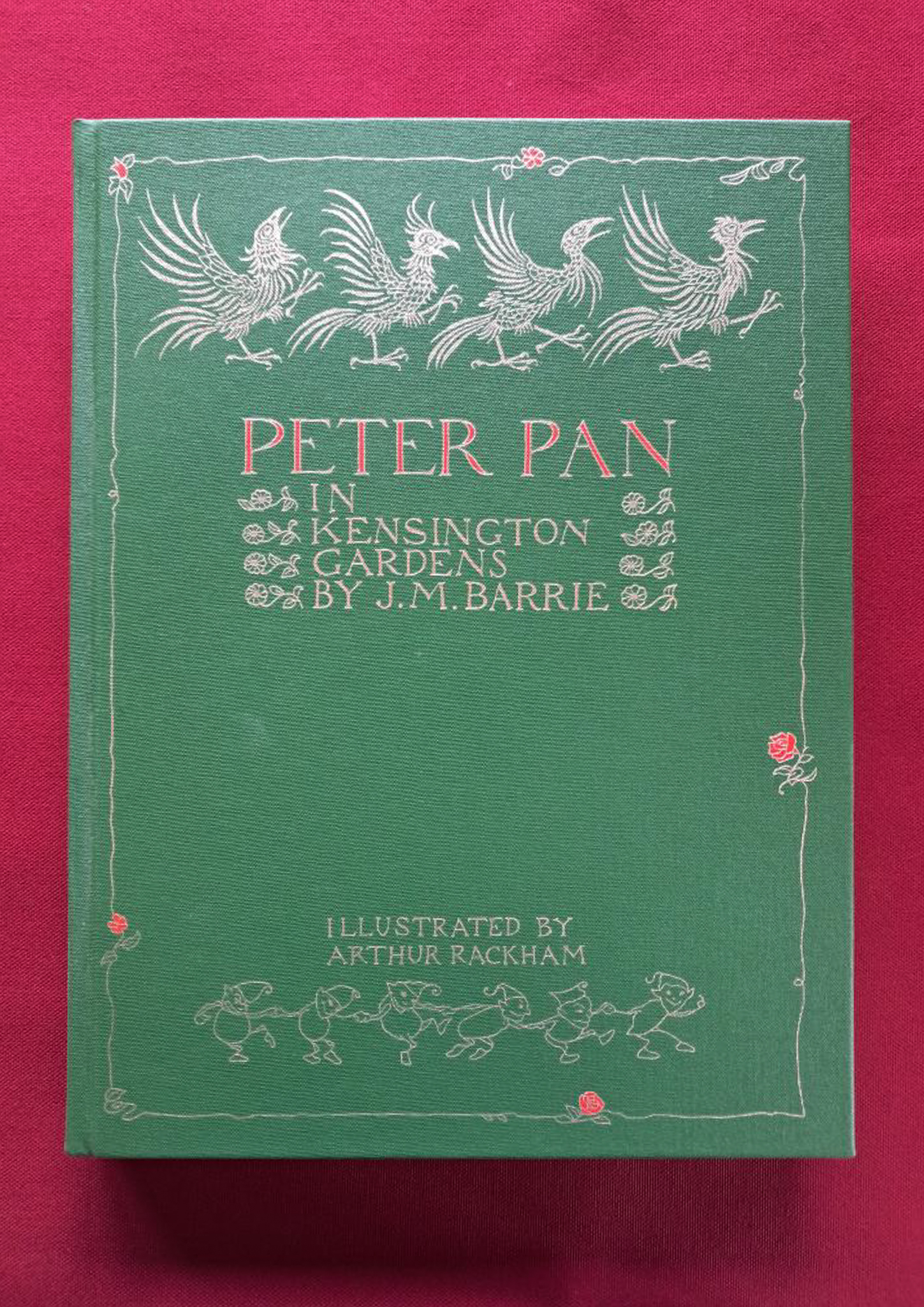 Peter Pan in Kensington Gardens. A dark green cover with silver writing, set on a red background