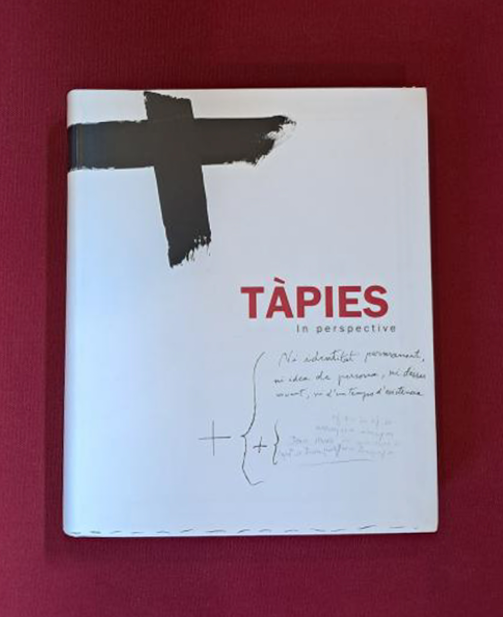 Tapies: In Perspective. A white cover with a black cross on the upper left. Set on a dark red background