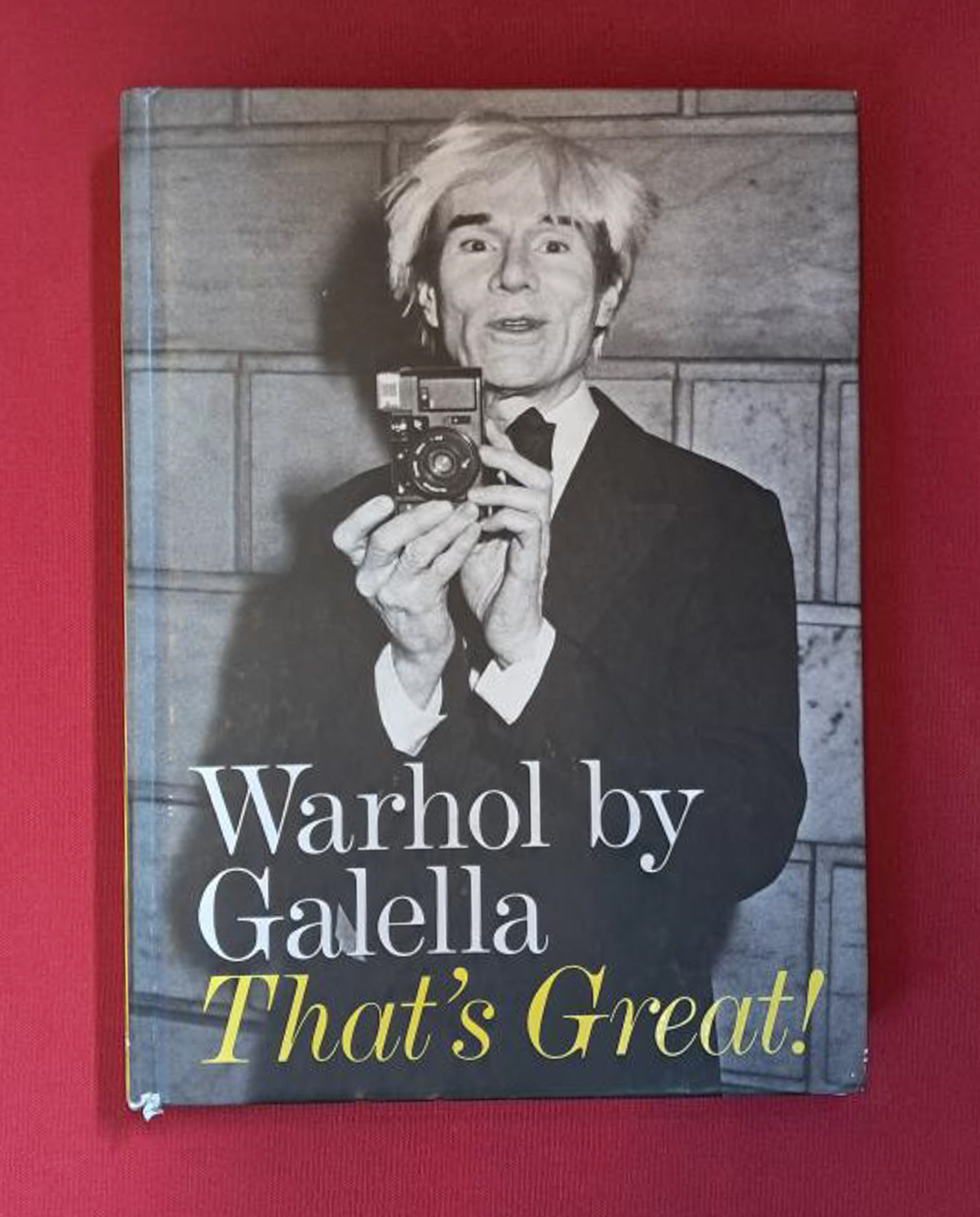 Warhol by Galella: That's Great. Cover image shows a black and white photo of a man face on, holding a flash camera. The book is set on a dark red background