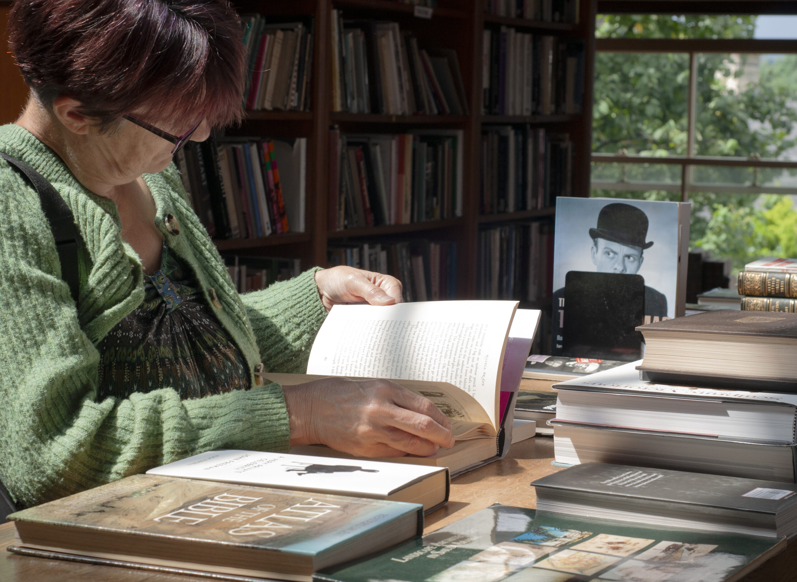 A woman wearing a green cardigan is holding a book open, resting it on a counter. You cannot see her face